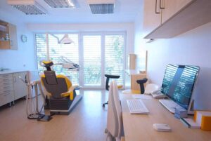 Modern dental office with a dental chair and desk near large windows.
