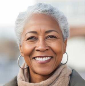 An older woman with restored teeth smiling confidently while standing outside.
