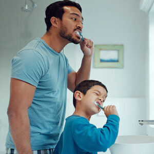 An adult and child brushing their teeth to prevent gum disease.