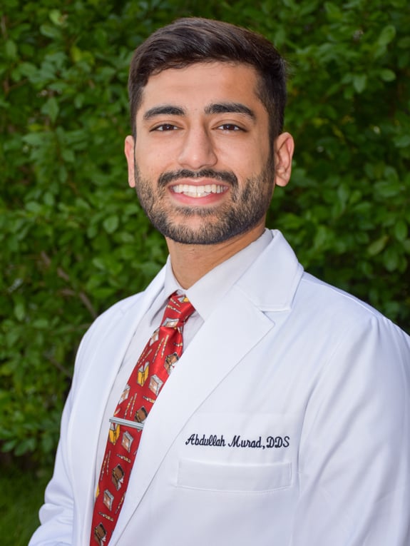 Lewisville, TX dentist Dr. Muhammad Murad smiles for a headshot in a white shirt and red tie