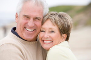 A mature couple smiling together on a beach after restorative dentistry in Lewisville.